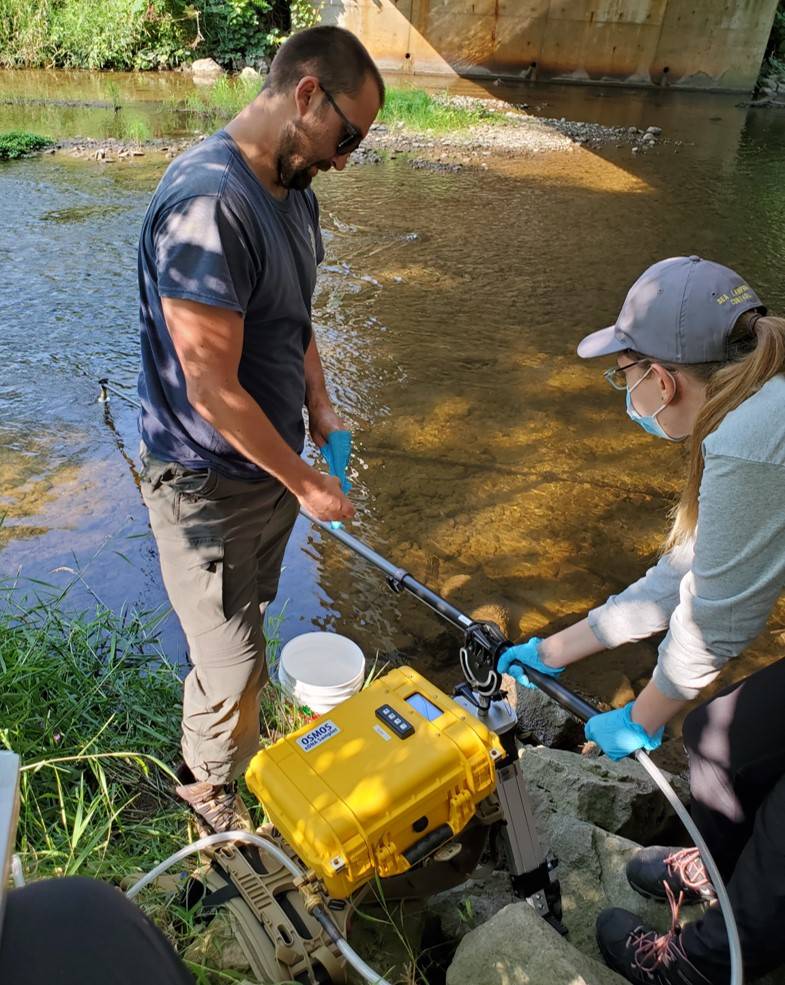 Two people at side of river with automated eDNA sampler